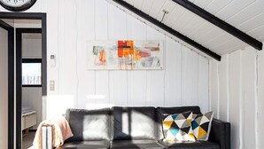 Een moderne woonkamer met een zwarte leren bank, een kussen met een geometrisch patroon en twee kleine witte tafels.