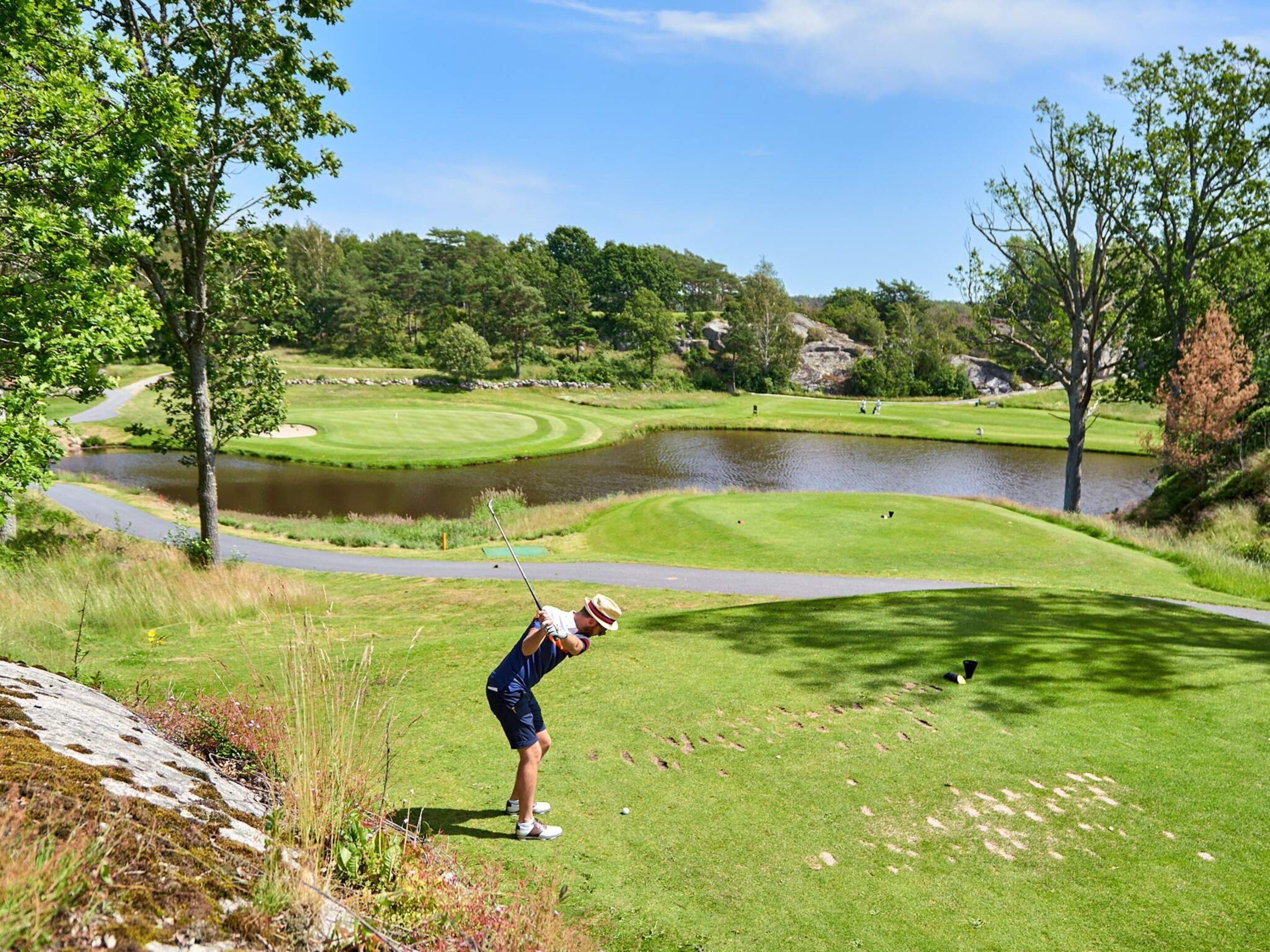 A golf course with a pond, trees, and a clear sky.