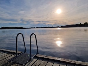 A wooden dock with metal railings extending into calm water, reflecting the sun.