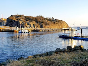A coastal scene with a dock, a small boat, and a rocky hill in the background.
