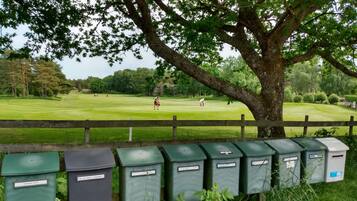 A golf course with a wooden fence and green waste bins labeled with names.