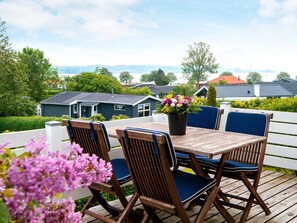 A wooden deck with a table and chairs, a potted plant, and a view of houses and trees. - 6 Person Holiday Home in Broager (Broager)