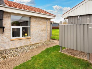 A house with a brick exterior, a window with a view, a small garden area with grass and gravel, and a grey fence. - 6 Person Holiday Home in Broager (Broager)
