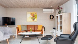 Een moderne woonkamer met een bank, salontafel en stoelen. Er is een flatscreen-televisie, een schilderij en een kast met glazen deuren.