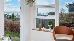 Een kamer met een groot raam dat uitkijkt op een prachtig landschap, een klein tafeltje met een stoel en een hangende plant.