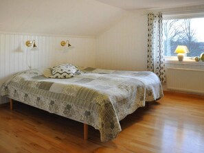 A bedroom with a bed, a window with curtains, and a lamp on the windowsill.