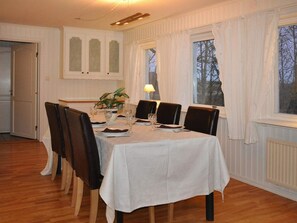 Ruokailuhuone, jossa on neljälle katettu ruokapöytä, tuolit, ruukkukasvi ja ikkuna, jossa on verhot.
