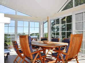 A sunlit dining area with a round wooden table surrounded by wooden chairs with blue cushions.