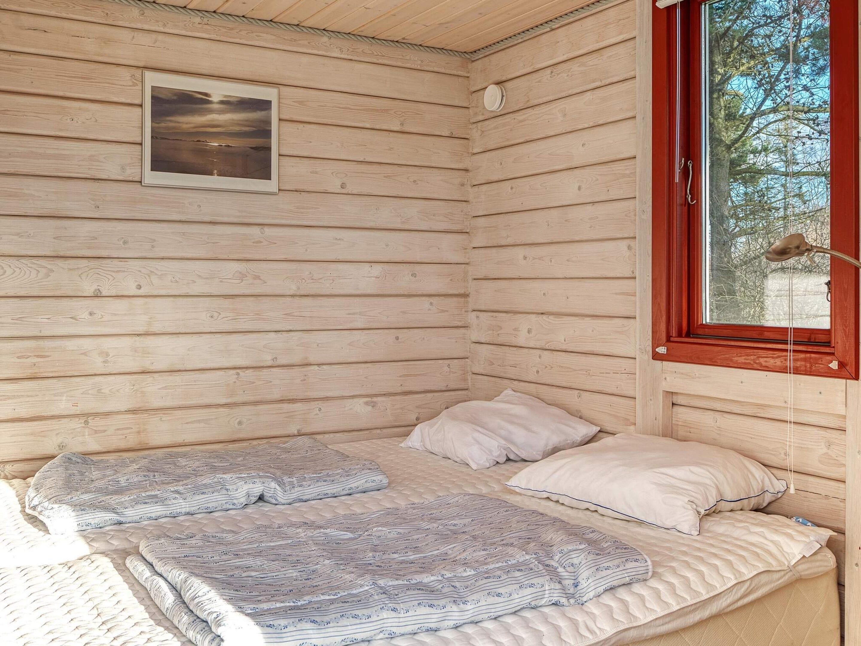 A small wooden cabin room with a bed, a window, and a picture on the wall.