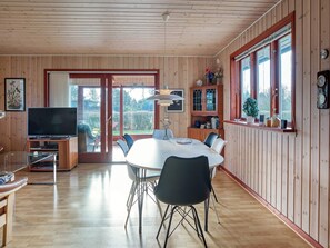 A wooden-paneled room with a dining table, chairs, a television, and a bookshelf.
