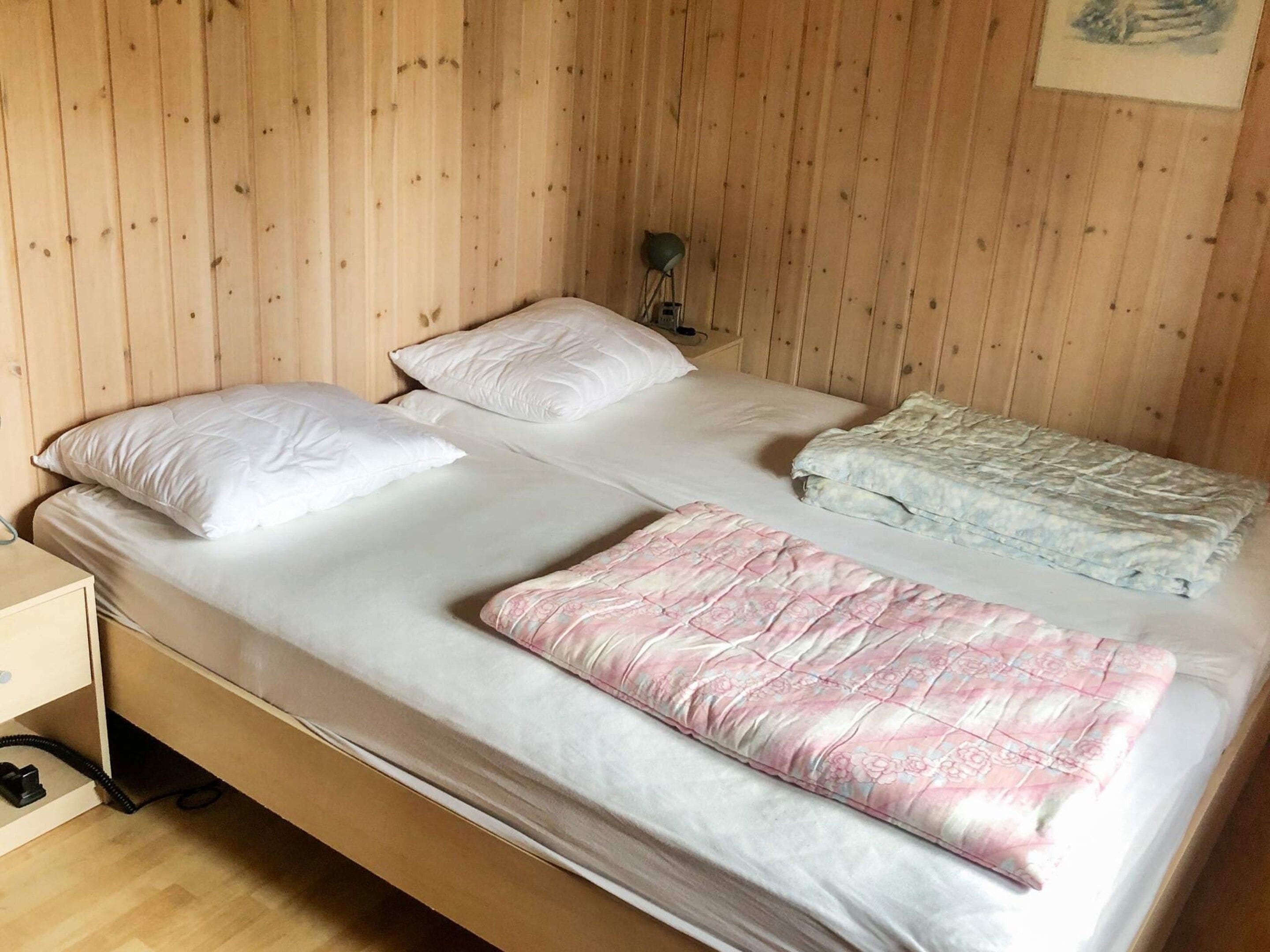 Un lit simple avec une literie blanche et rose, une tête de lit en bois et une table de chevet avec une lampe.