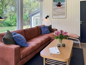 A modern living room with a brown leather sofa, a wooden coffee table, and a view of the outdoors through large windows. - 12 Person Holiday Home in Fano (Fano)
