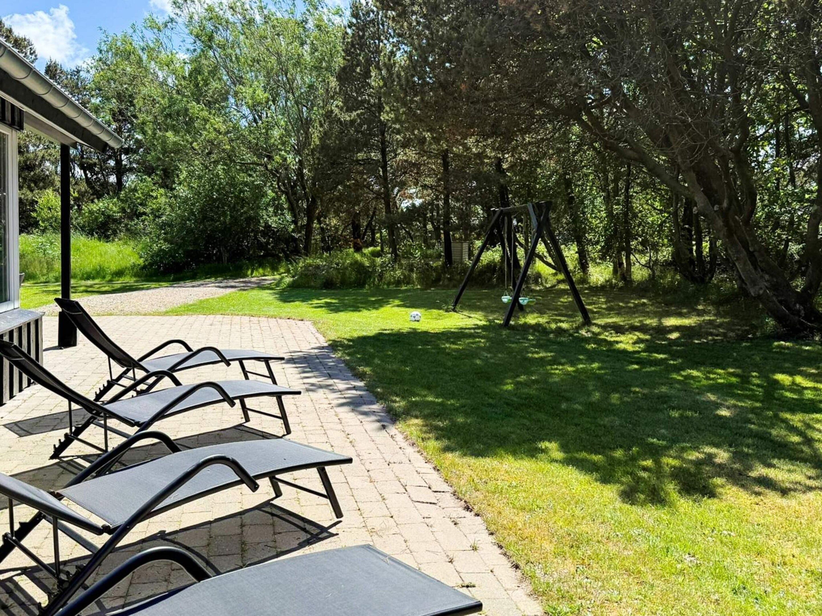 Une terrasse avec des fauteuils de jardin, une balançoire et une pelouse avec des arbres.