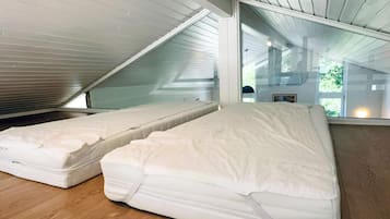A room with two mattresses on the floor, a sloped ceiling, and a large window.
