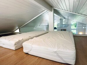 A room with two mattresses on the floor, a sloped ceiling, and a large window.