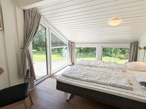 Ett sovrum med en stor säng, en stol och utsikt över naturen.