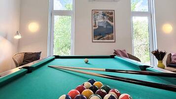 A pool table with balls, a framed picture, and a window with a view of greenery.