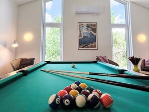 A pool table with balls, a framed picture, and a window with a view of greenery.