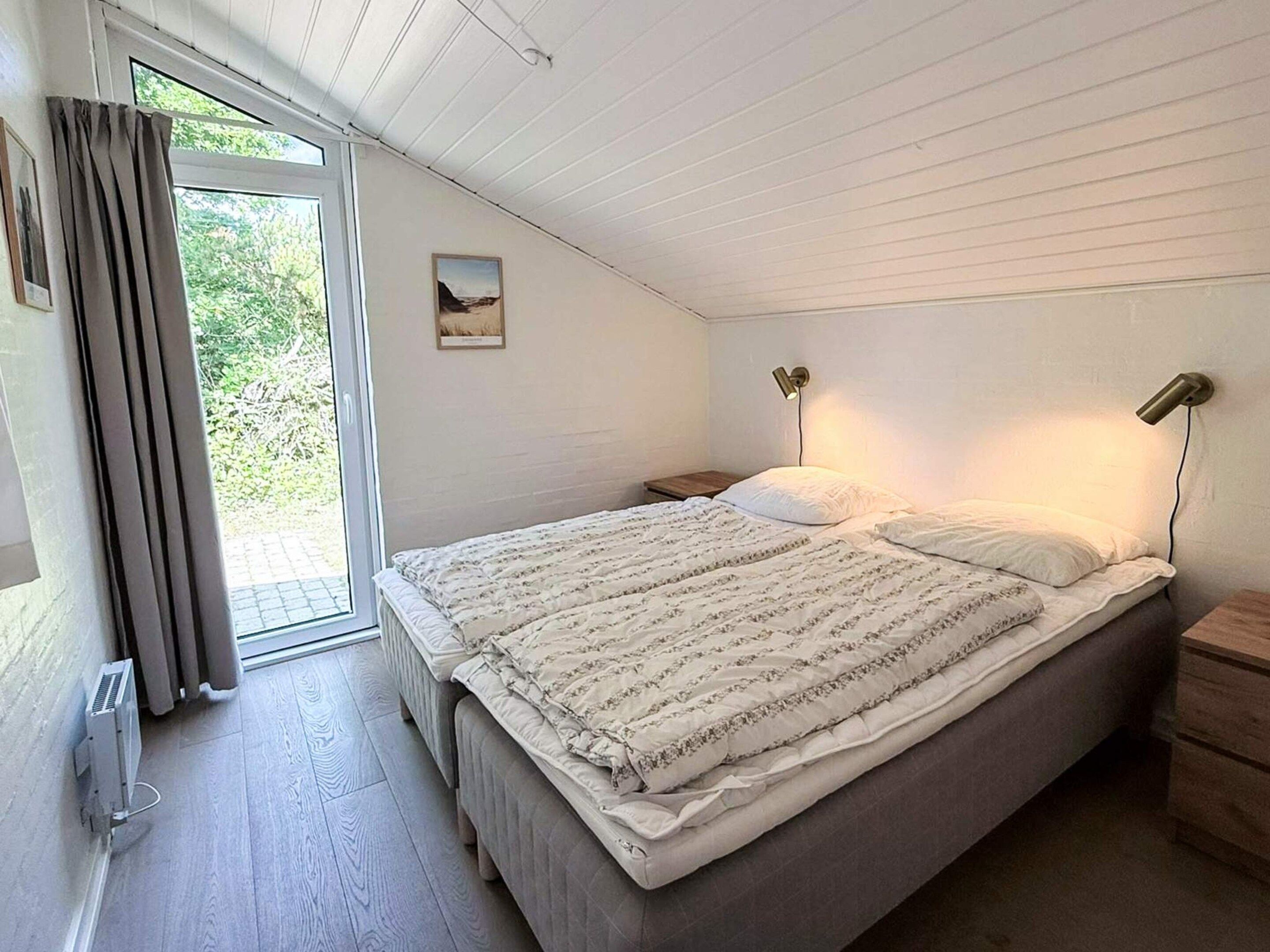 A bedroom with a large bed, two bedside lamps, a nightstand, a window with curtains, and a radiator.