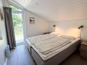 A bedroom with a large bed, two bedside lamps, a nightstand, a window with curtains, and a radiator.