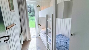 Una habitación con literas, una puerta con picaporte, una ventana y vista a la vegetación exterior.