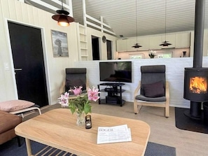 A cozy living room with a flat-screen TV, comfortable seating, a wooden coffee table, and a wood-burning stove.