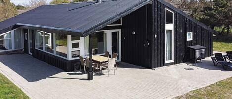 A modern building with a black exterior, large windows, and a patio area with outdoor seating.