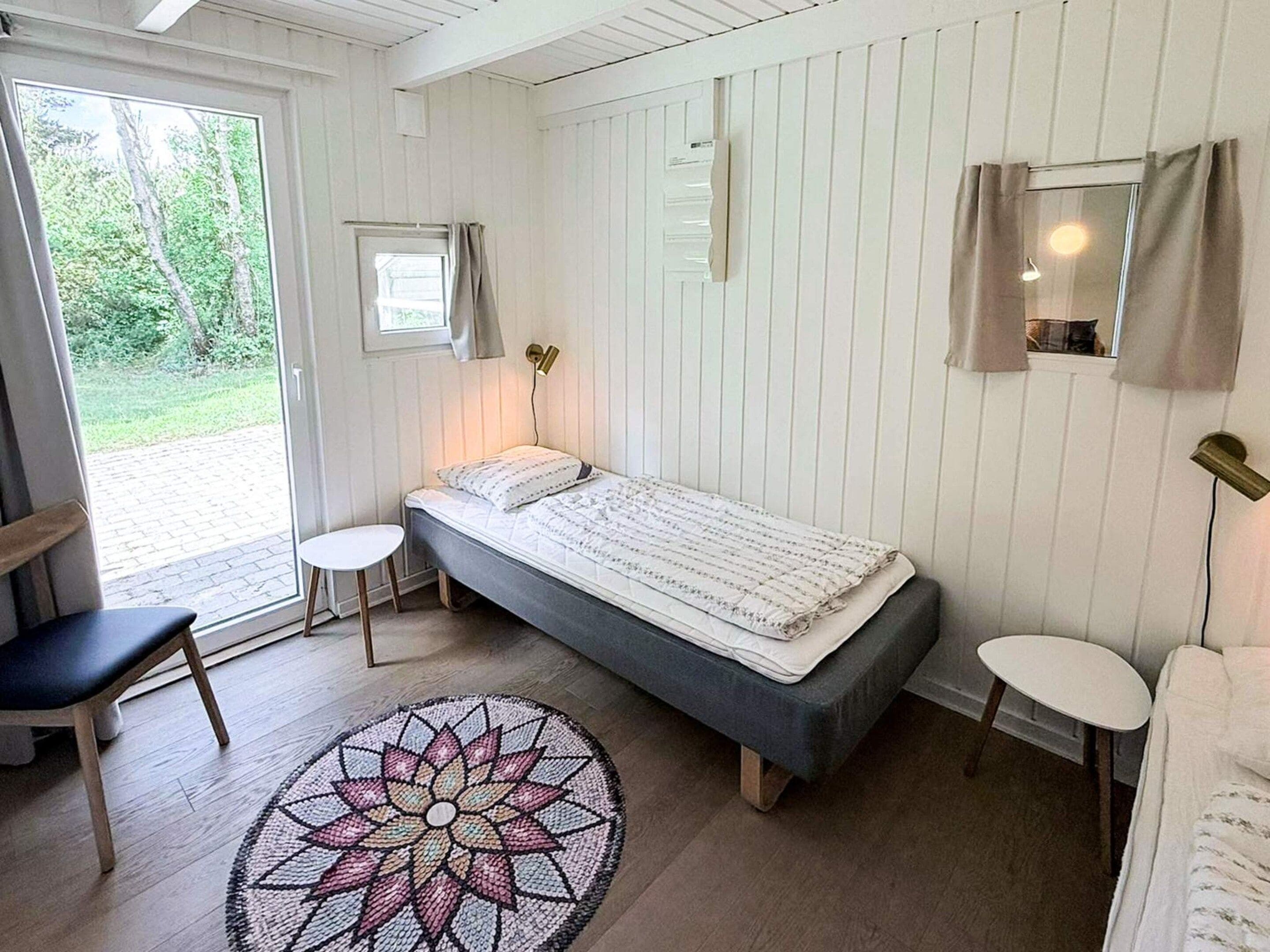 Una habitación con cama, dos sillas, una mesita, una ventana con cortinas y una puerta que da al exterior.