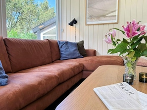 A brown leather sofa with a blue pillow, a wooden table with a newspaper, and a vase with flowers. - 12 Person Holiday Home in Fano (Fano)