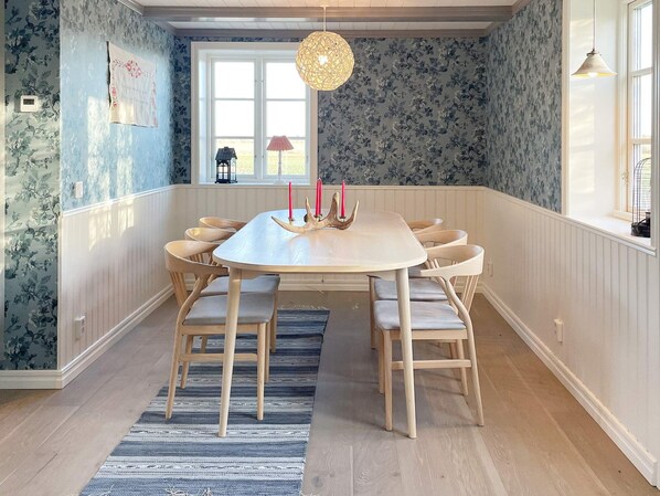 A dining area with a round table, wooden chairs, a striped rug, and a window with a view.