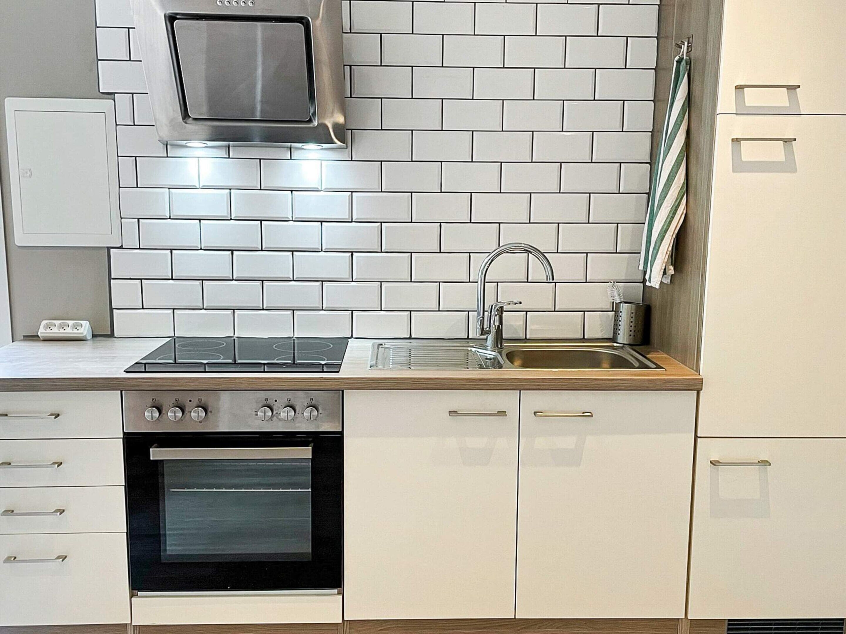A modern kitchen with white cabinetry, a stainless steel range hood, a built-in oven, and a sink.