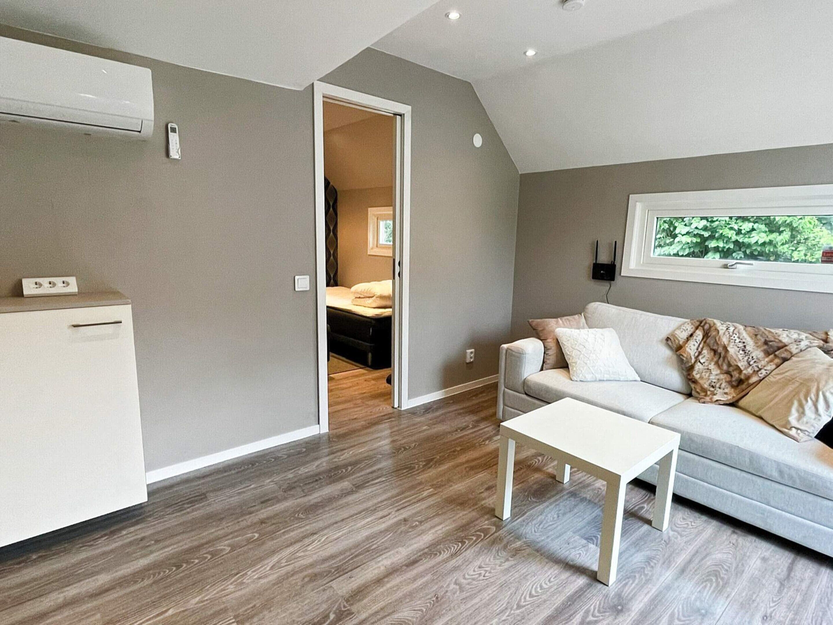 A compact living space with a kitchenette, a sofa, a coffee table, and a window with a view of greenery.