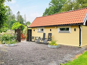 A yellow building with a red-tiled roof, a gravel driveway, and outdoor seating with chairs and tables. - 4 Star Holiday Home in Farlov (Färlöv)