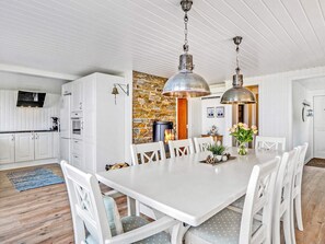 A modern kitchen with white cabinetry, a stone accent wall, and a dining area with a white table and chairs.