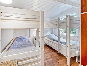 A bunk bed room with a wooden floor, white walls, and a window providing natural light.