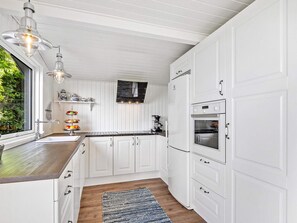 A modern kitchen with white cabinetry, a built-in oven, and a window overlooking greenery. - 5 Star Holiday Home in Vinderup (Vinderup)