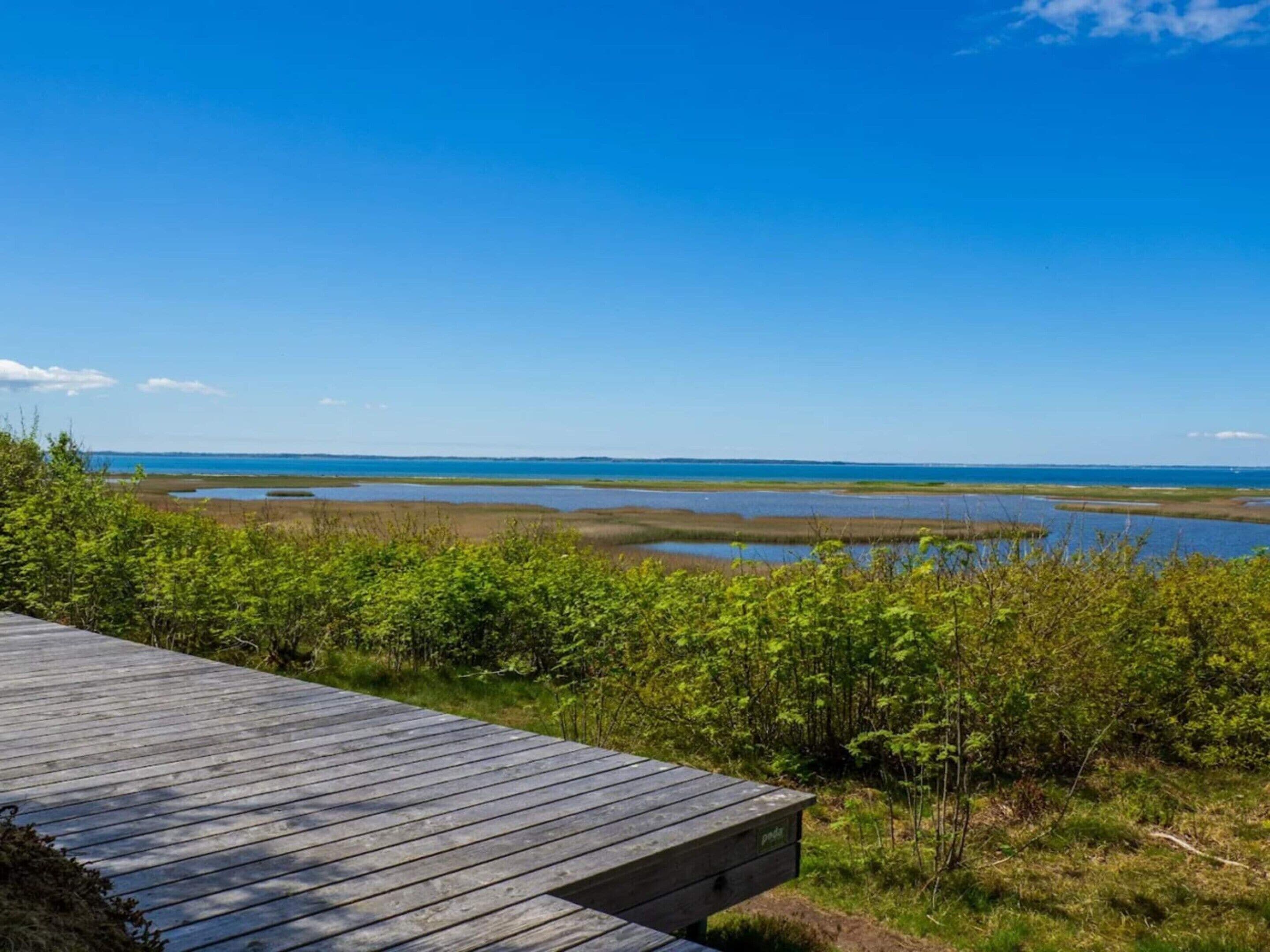 A wooden deck overlooking a coastal landscape with marshy areas and a clear blue sky.