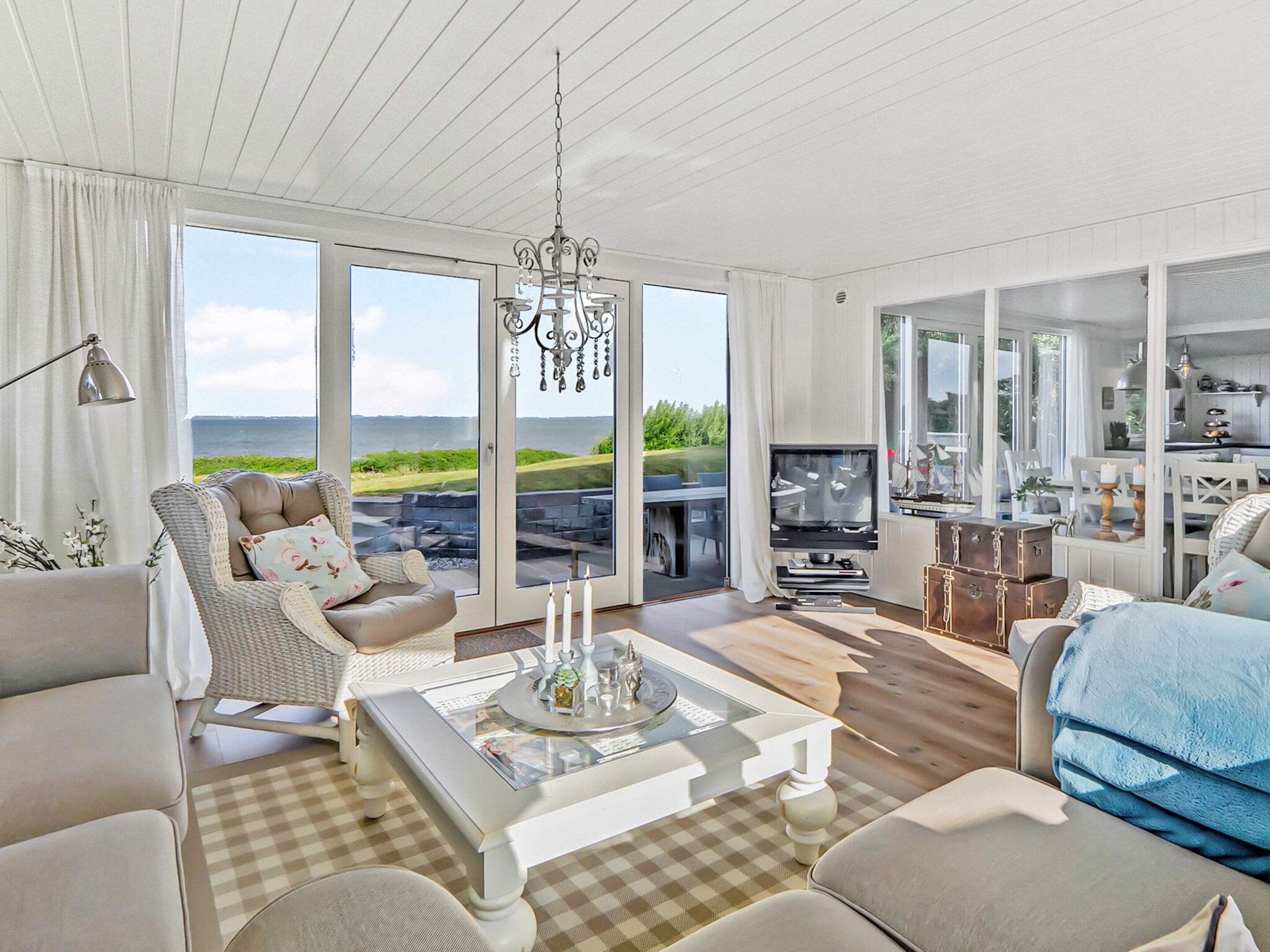 A spacious living room with a large window, a chandelier, a television, and a dining area.