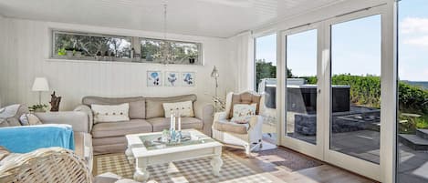 A spacious living room with a large window, a sofa, a coffee table, and a wicker chair.