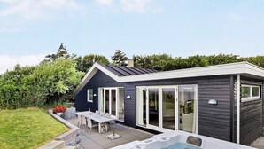 Une maison moderne dotée d’un jacuzzi, d’une terrasse avec mobilier d’extérieur et d’une grande porte-fenêtre coulissante.