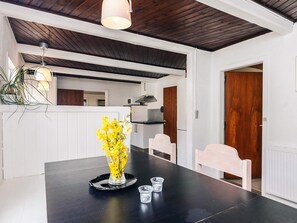A modern kitchen with white cabinets, a wooden ceiling, and a dining area with a black table and chairs.