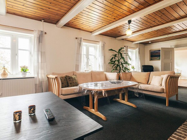 A room with a wooden ceiling, a beige sofa, a round table, and a large window.