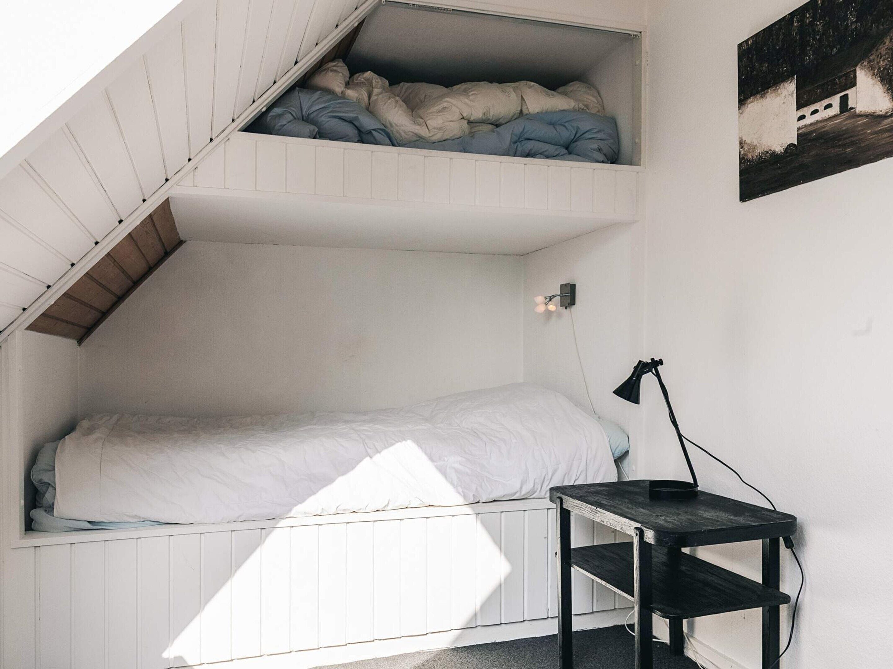 Habitación tipo dormitorio con cama elevada, escritorio y lámpara de pared.