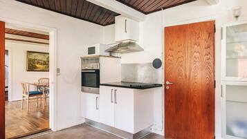A compact kitchen with white cabinets, a built-in oven, and a microwave. There's a wooden door and a glass cabinet to the right.