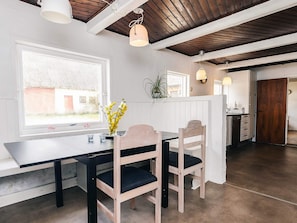 A dining area with a table and chairs, a window with a view, and a kitchen area in the background. - 4 Star Holiday Home in Aabybro (Aabybro)
