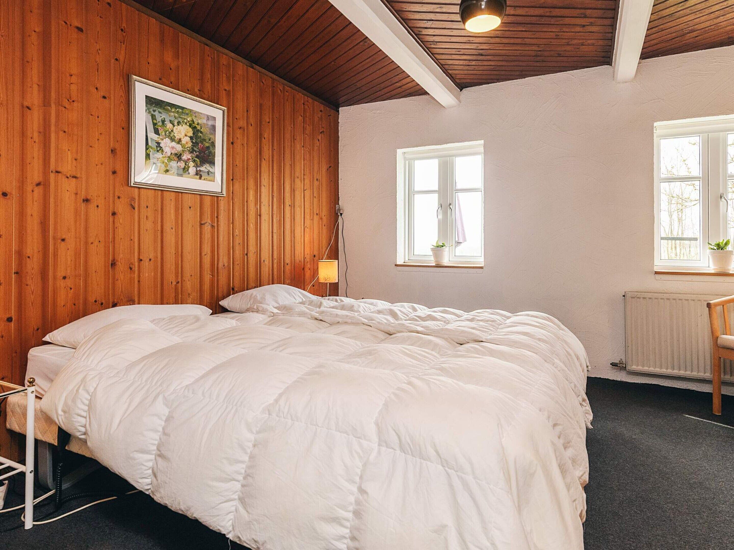 Une chambre avec un mur en bois, un lit avec une literie blanche, une lampe de chevet et une fenêtre avec une plante.