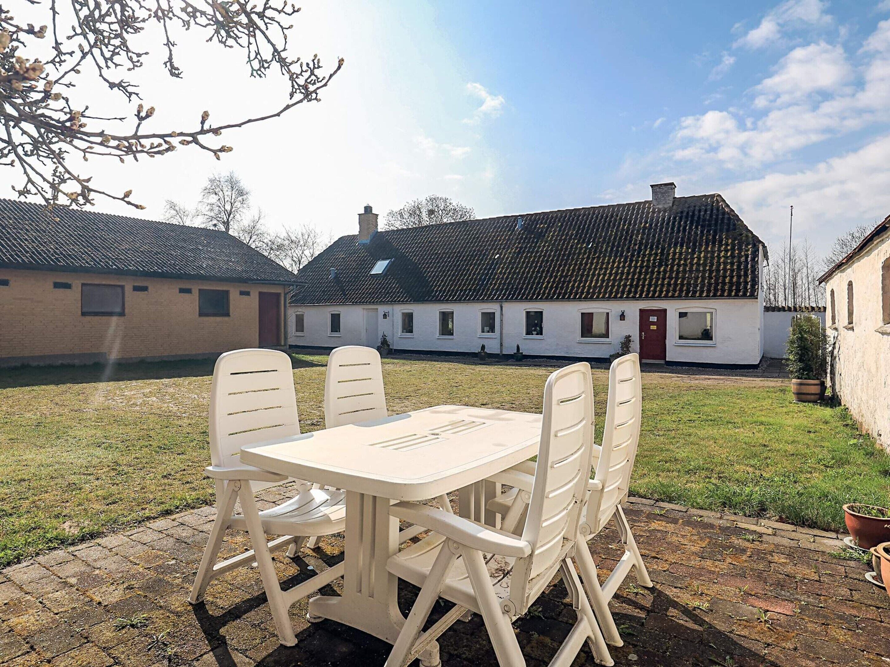 A patio with a table and chairs, a grassy lawn, and a white building with a red door in the background.