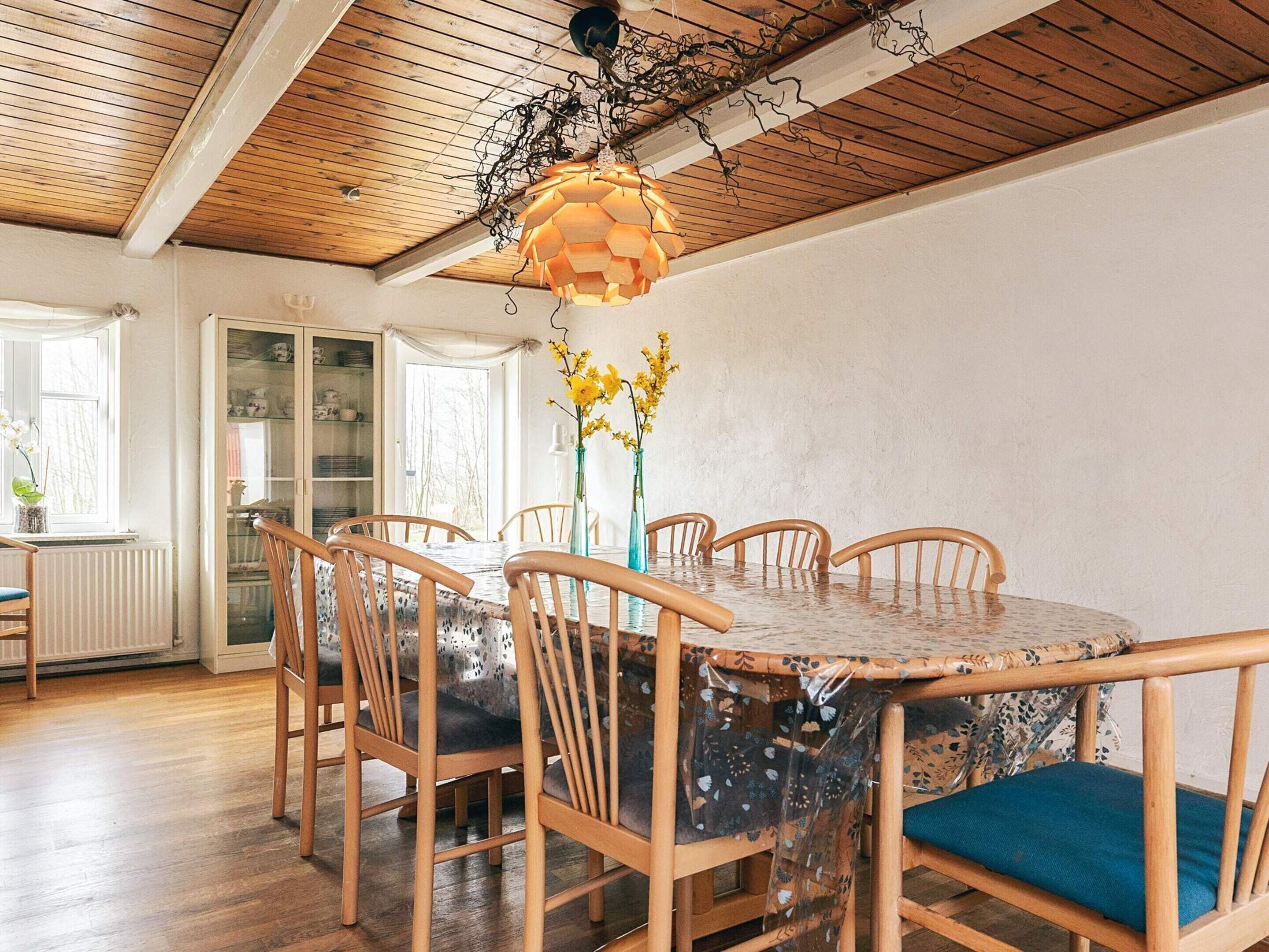 Comedor con una mesa redonda, seis sillas de madera y una lámpara colgante.