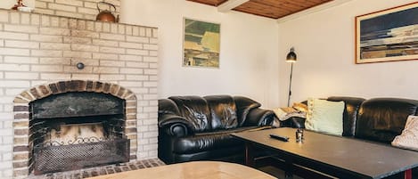 A cozy living room with a brick fireplace, leather sofas, a wooden coffee table, and a painting on the wall.