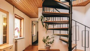 A spiral staircase with wooden steps and metal railings, a white radiator, a wooden bench with a potted plant, and a wooden dresser with drawers.